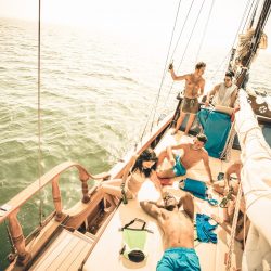 Happy multiracial friends having fun at sail boat trip party with dj set - Friendship concept with young multi racial people on sailboat - Travel lifestyle on exclusive location - Warm retro filter