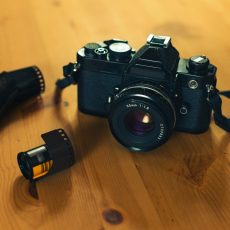 Still life image of an analog camera with some 35mm negative film  on a wooden background.